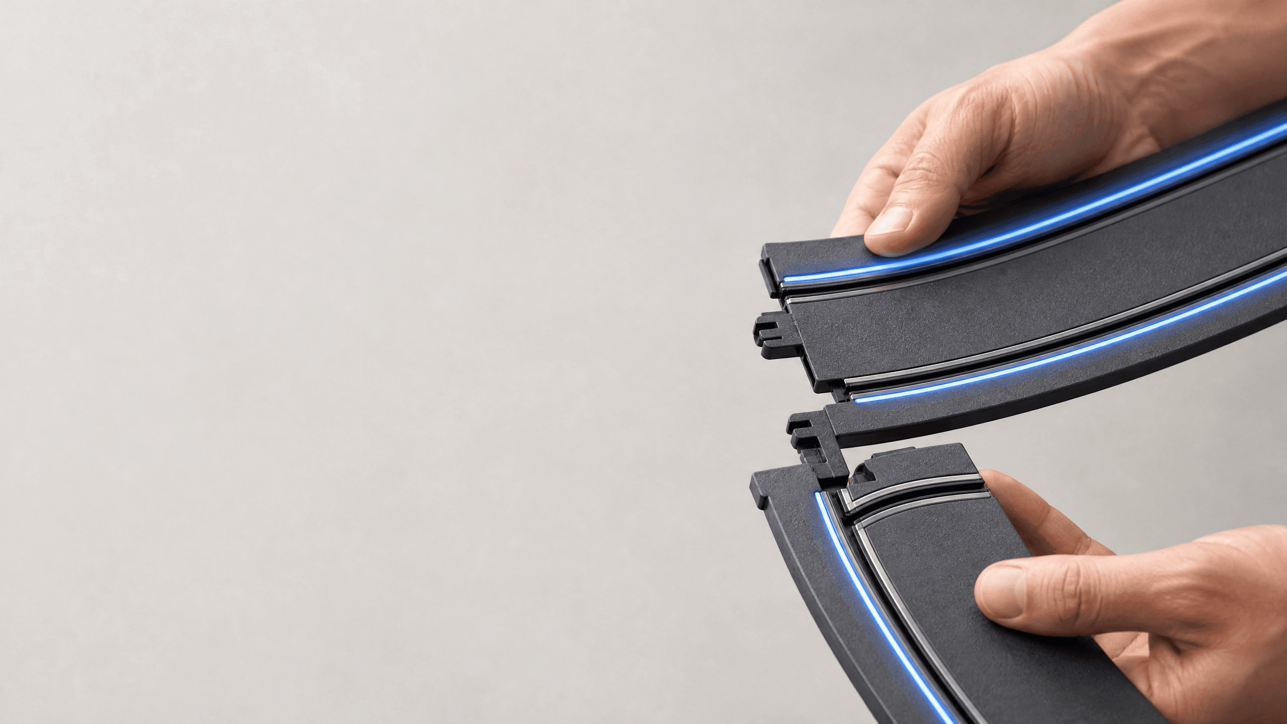 Mãos conectando duas peças de pista modular Vitrack, friso de luz azul